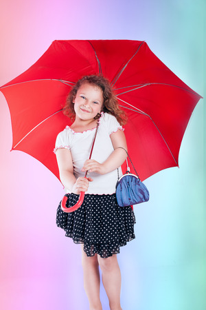 Pretty little girl posing with red umbrella over rainbow background  の写真素材