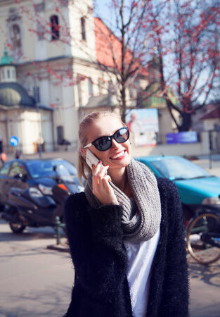 Fashionable young blonde woman talking by phone on street, sunny day. Girl smiling.の写真素材