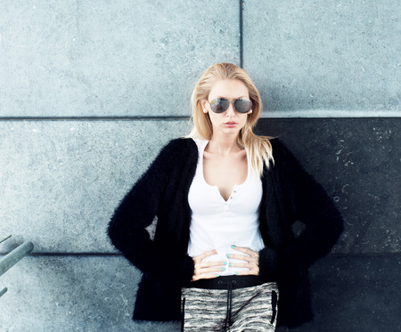 Young beautiful fashionable blonde woman posing over wall, wearing sunglasses.の写真素材