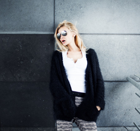 Young beautiful fashionable blonde woman posing over wall, wearing sunglasses.の写真素材