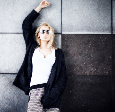 Young beautiful fashionable blonde woman posing over wall, wearing sunglasses.の写真素材