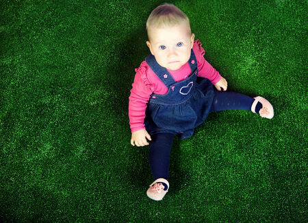 Cute little baby girl posing in studio over green grass background.