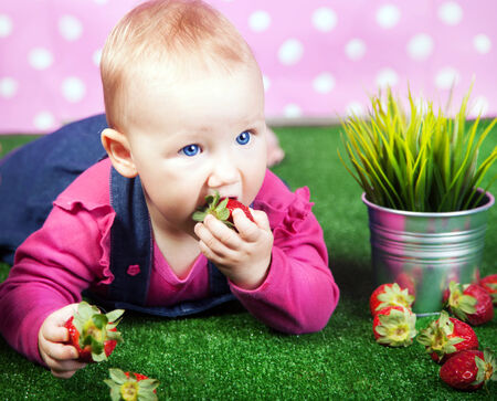 Small cute baby girl lying on grass, posing with strawberries.の写真素材