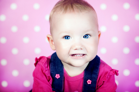 Small cute baby girl looking at camera over pink background. Portrait.の写真素材