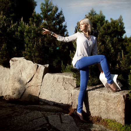 Young fashionable beautiful girl posing in sunny day in park, wearing blue jeans.の写真素材
