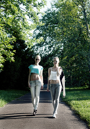 Happy two best friends walking in park. Summer sunny day. Fashionable girls smiling.の写真素材