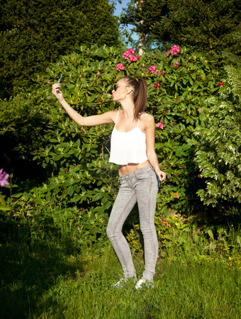 Beautiful young brunette girl posing, doing selfie over green summer garden in sunny day.の写真素材