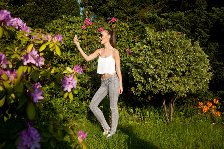 Beautiful young brunette girl posing, doing selfie over green summer garden in sunny day. の写真素材