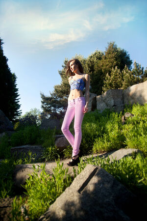 Fashionable beautiful young woman posing outdoor in park, summer day. Girl wearing pink jeans. Brunette lady.の写真素材