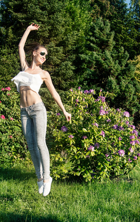 Beautiful young brunette girl jumping over green garden background. Happy woman, summer time.の写真素材