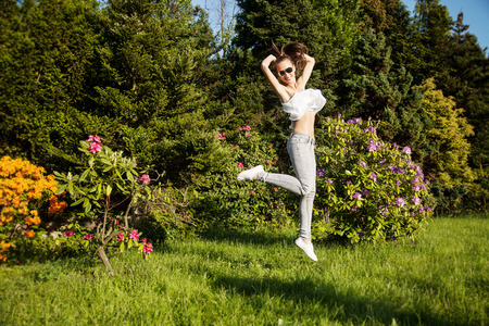 Beautiful young brunette girl jumping over green garden background. Happy woman, summer time.の写真素材