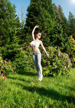 Beautiful young brunette girl jumping over green garden background. Happy woman, summer time.の写真素材