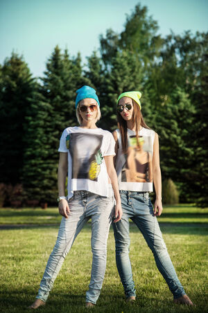 Two young beautiful girls posing outdoor in park, wearing fashionable clothes. Summer photo. Best friends.の写真素材