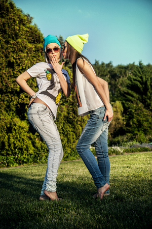 Two young beautiful girls posing outdoor in park, wearing fashionable clothes. Summer photo. Best friends.の写真素材