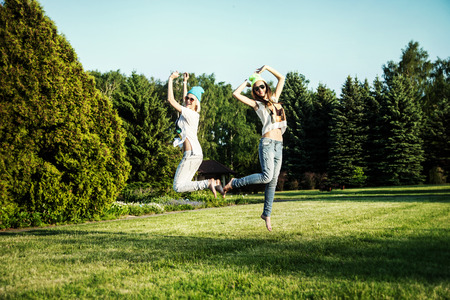 Two young beautiful girls jumping in park, wearing fashionable clothes. Summer photo. Best friends.の写真素材