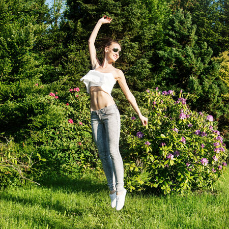 Beautiful young brunette girl jumping over green garden background. Happy woman, summer time.の写真素材