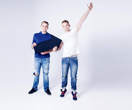 Two young fashionable man posing in studio with black empty arrow, showing dollars lettering, smiling. Conceptual photo.の写真素材