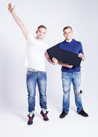 Two young fashionable man posing in studio with black empty arrow, showing dollars lettering, smiling. Conceptual photo.の写真素材