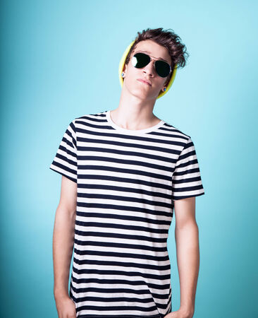 Young fashionable handsome guy posing wearing sunglasses. Studio photo. Blue background.の写真素材