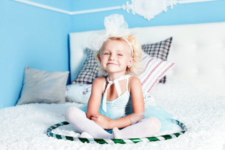 Pretty little blonde girl sitting on big bed, looking at camera, playing.の写真素材