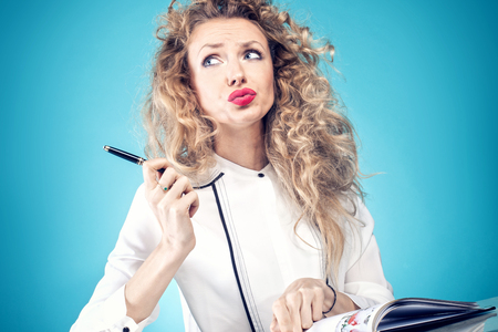 Attractive businesswoman at work. Girl with blonde long curly hair. Blue background.の写真素材