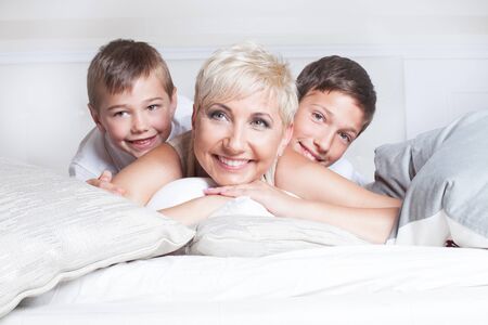 Family portrait. Smiling beautiful mother lying in bed with two sons, relaxing. Happy people.の写真素材