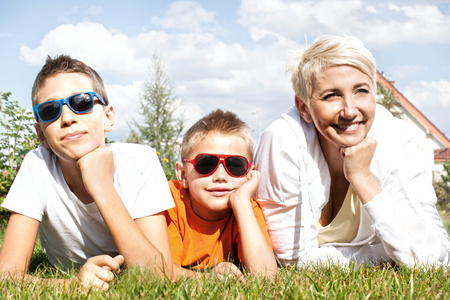 Portrait of happy family. Beautiful mother with two young sons enjoying suuny day, lying on the grass.の写真素材