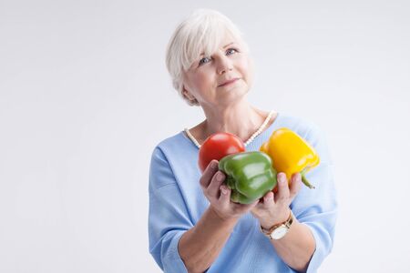 Good looking senior woman holding fresh vegetables in hand. Healthy lifestyle concept.の写真素材