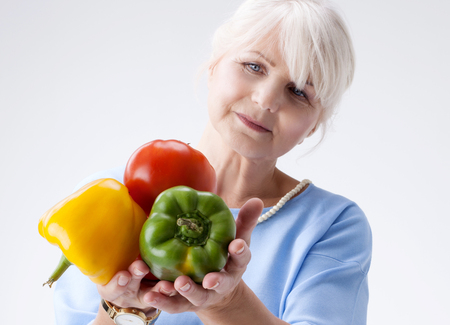 Good looking senior woman holding fresh vegetables in hand. Healthy lifestyle concept.の写真素材
