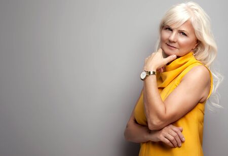 Portrait of beautiful fashionable senior woman with long grey hair. Lady wearing yellow dress, looking at camera. Studio shot.の写真素材