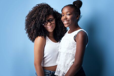Two beautiful african american girls smiling, looking at camera. Sisters posing on blue background. Studio shot.の写真素材