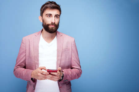 Young elegant handsome man using mobile phone. Studio shot. Blue background.の写真素材