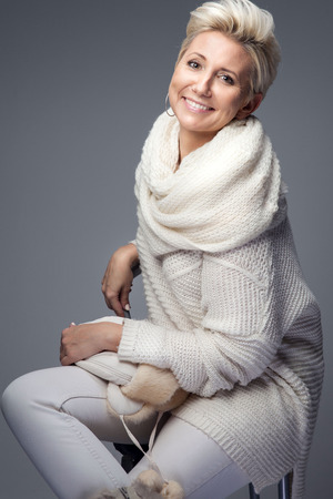 Beautiful adult blonde woman with short hair posing in studio, smiling. Lady wearing sweater and scarf.の写真素材