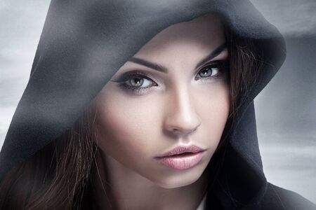 Closeup beauty portrait of attractive young woman with beautiful brown eyes. Hood on head. Brunette girl. Studio shot.の写真素材