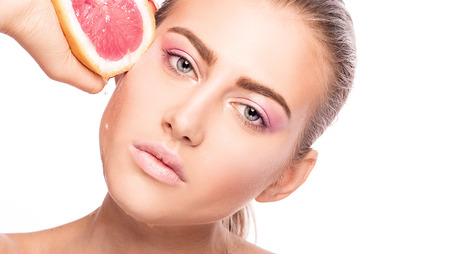 Closeup beauty portrait, young beautiful girl with ideal skin and delicate makeup. Girl holding fresh grapefruit in hand. Studio shot.の写真素材