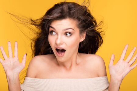 Beauty portrait of young attractive brunette woman with long hair and natural makeup. Yellow background. Studio shot. Emotions.の写真素材