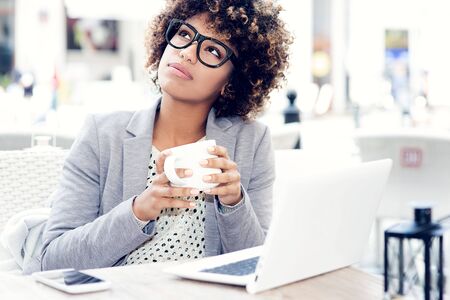 Photo of beautiful woman sitting at cafe. Young african american woman sitting in a coffee shop and working on laptop.の写真素材