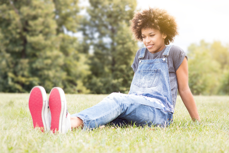 Young pretty african american girl relaxing in park, lying on green grass. Girl smiling. Leisure time. Outdoor shot.の写真素材