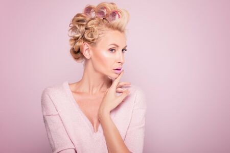 Beauty potrait of young blonde woman with glamour makeup and hot rollers. Pink background. Beauty concept.の写真素材