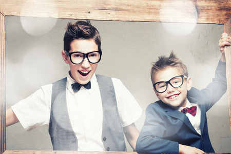 Portrait of two young elegant brothers posing in wooden frame, looking at camera, wearing...