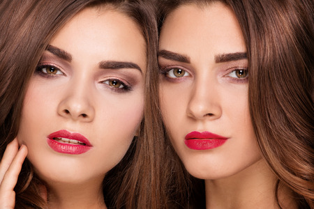 Fashion studio photo of two beautiful young ladys . Beauty portrait of twins sisters. Perfect face makeup.の写真素材