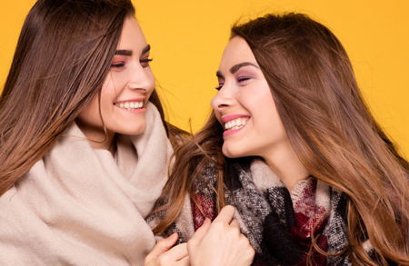 Cheerful beautiful young twins sisters posing on yellow background. Autumn, winter style.の写真素材