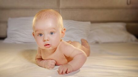 Adorable little baby boy lying on tummy in white bed.