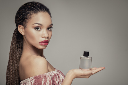 Beauty portrait of young african american girl holding bottle of perfume, looking at camera.の写真素材