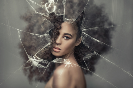Beauty portrait of sensual african american woman with long curly hair , looking through broken glass.の写真素材