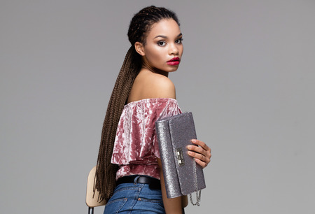 Beautiful african american girl posing in fashionable clothes, holding bag.の写真素材