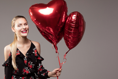 Beautiful blonde smiling woman holding red balloons, looking at camera, valentine's day.の写真素材