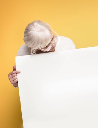 Happy beautiful senior woman holding empty board, yellow background.の写真素材