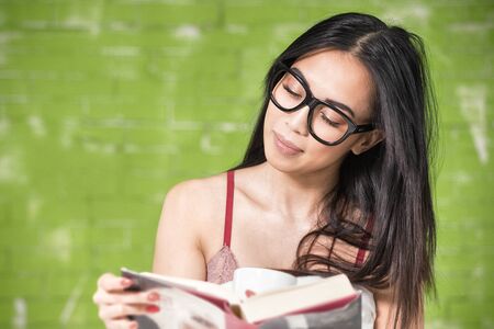 Beautiful young asian woman reading book, holding a cup of tea. Leisure time at the morning.