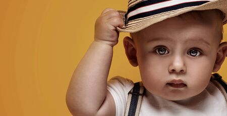 Cute baby boy posing in summer hat on yellow background. Adorable little child in studio.の写真素材